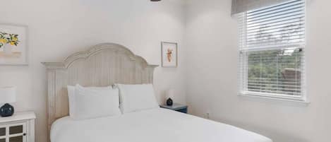 A bedroom with a bed, a nightstand, a ceiling fan, a window with blinds, and wall art.