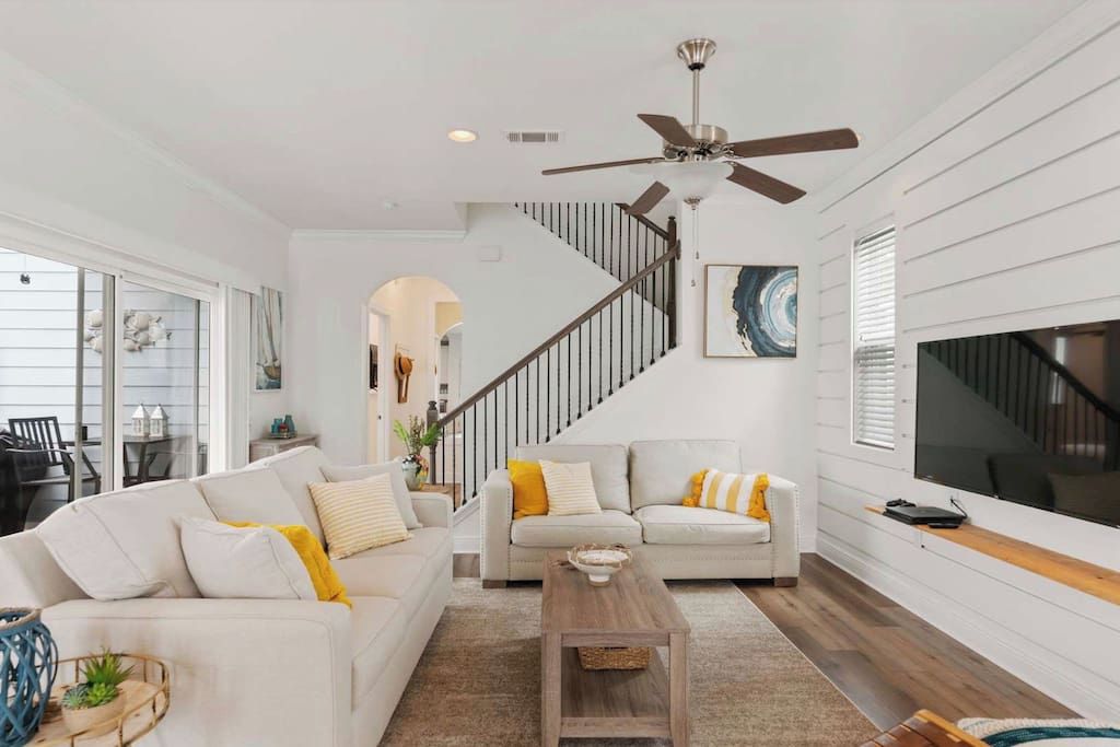 A spacious living room with a high ceiling, a ceiling fan, a staircase, and a large window.