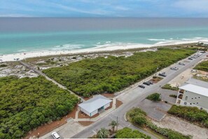 An aerial view of a coastal property with a beach, parking area, and a building with a flat roof.
