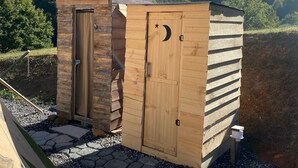 Ein Holler Schuppen mit Tür und Fenster, auf einem Kiesgrundstück vor Bäumen und Hügeln.