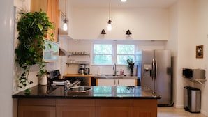 A modern kitchen with wooden cabinets, a stainless steel refrigerator, a coffee maker, and a potted plant. - Historic 5/4 • Spacious • Sleeps 16 • Hot Tub • Pool • A&M (Bryan)