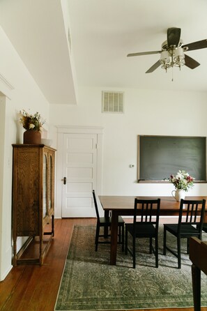 A dining area with a wooden table, black chairs, a green rug, a wooden cabinet, a ceiling fan, and a white door. - Historic 5/4 • Spacious • Sleeps 16 • Hot Tub • Pool • A&M (Bryan)
