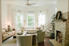 Ein Wohnzimmer mit Sofa, Sesseln, einem Couchtisch, einem Kamin und einer Treppe.
