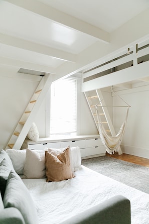 Ein Schlafzimmer mit einem Hochbett, einem Hängekorbstuhl und einem Fenster mit Jalousien.