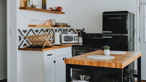 A compact kitchen with white cabinets, a black refrigerator, a microwave, and a wooden table with stools. - University District Guesthouse-Minutes to Nob Hill (Albuquerque)