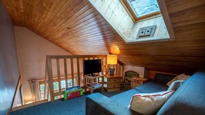 Ein gemütliches Schlafzimmer im Dachgeschoss mit Holzbalkendecke, Fernseher, Lampe und einer Couch.