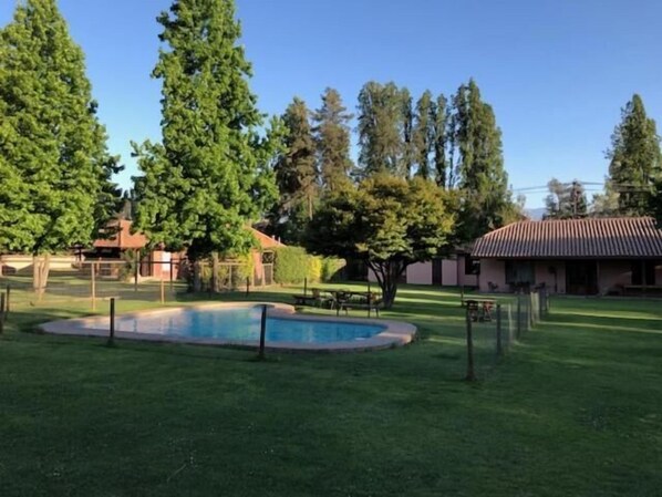 A swimming pool surrounded by a well-maintained lawn and tall trees. - Casa Los Ciervos (Pirque)