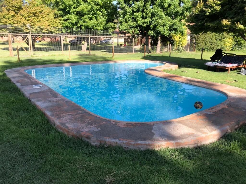 Ein rechteckiger Swimmingpool mit Holzdeckrand, umgeben von Gras und Bäumen.