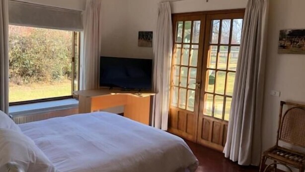 Hotellihuone, jossa on suuri sänky, televisio, työpöytä ja lasiovesta avautuva näkymä ulos.