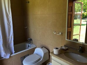 A bathroom with a bathtub, toilet, sink, and a mirror. - Casa Los Ciervos (Pirque)