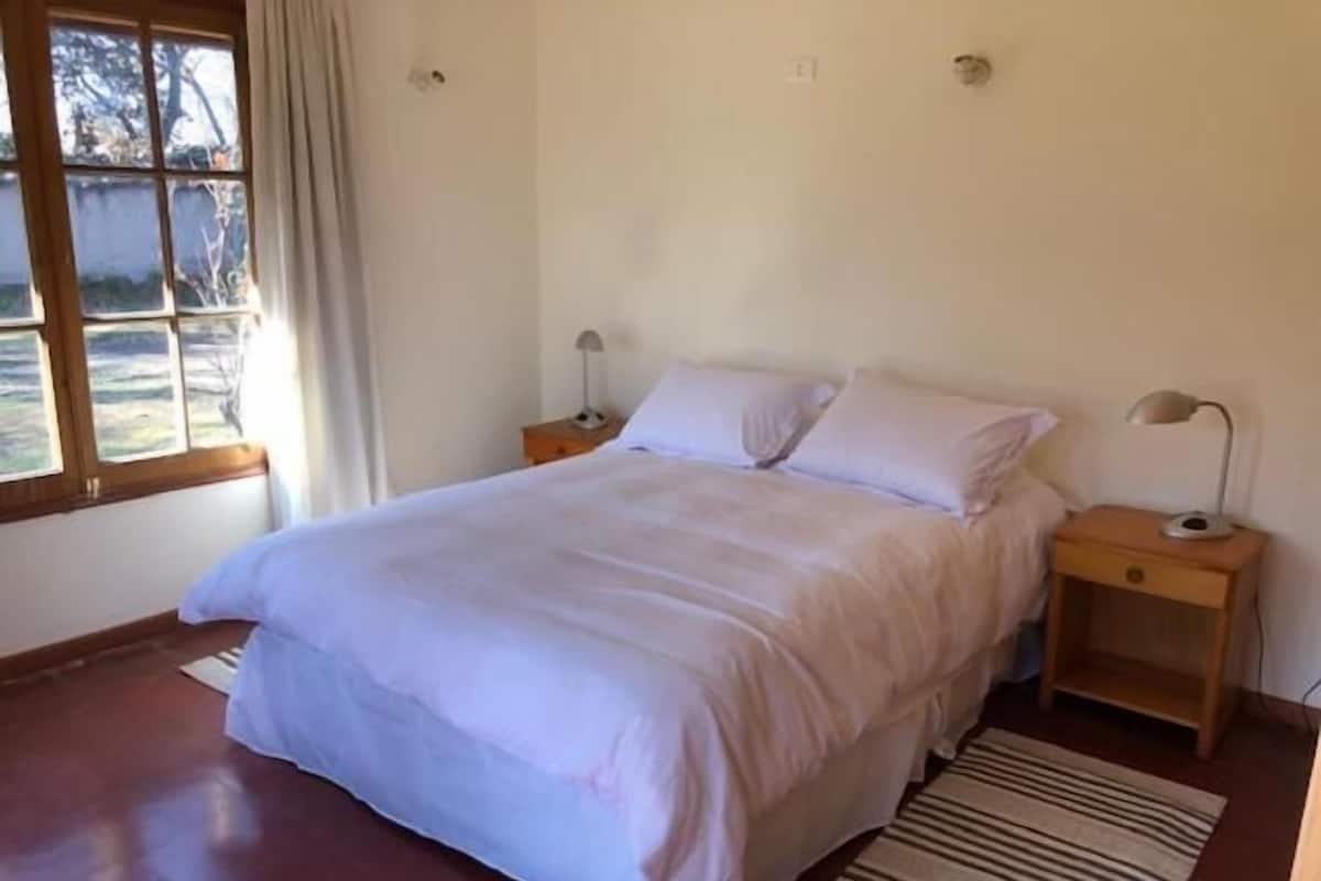 Un dormitorio con una cama, dos mesitas de noche, una ventana con cortinas y una alfombra a rayas.