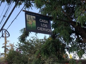 A sign with the text "CASA LOS CIERVOS" against a backdrop of dense foliage and a clear sky. - Casa Los Ciervos (Pirque)