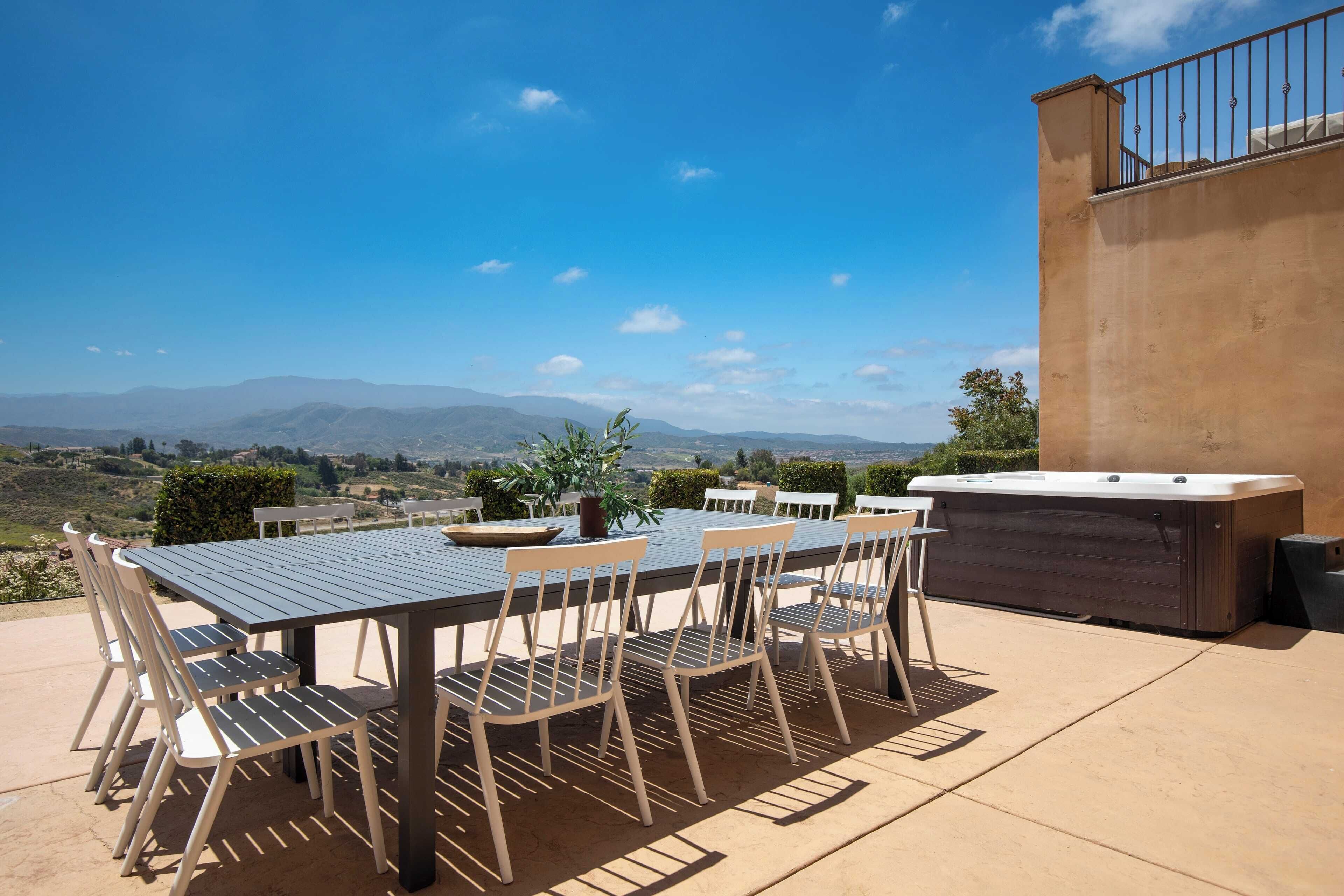 An outdoor patio with a table and chairs, a hot tub, and a scenic view of mountains.