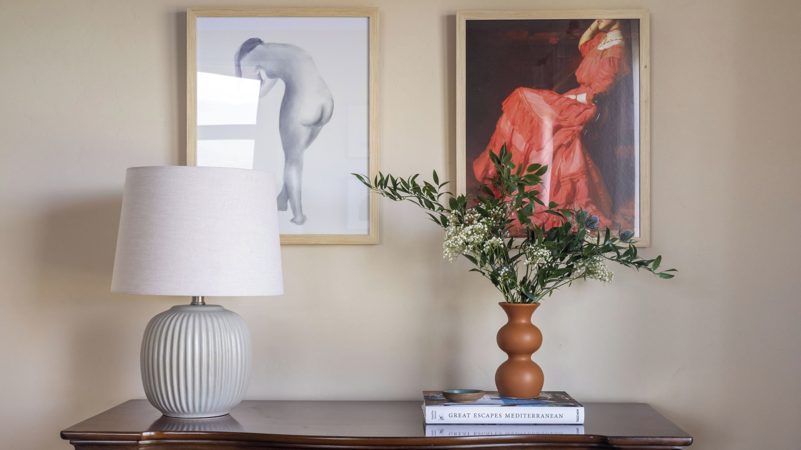 Une lampe, deux œuvres d’art encadrées, un vase avec des fleurs et une pile de livres sur une table.