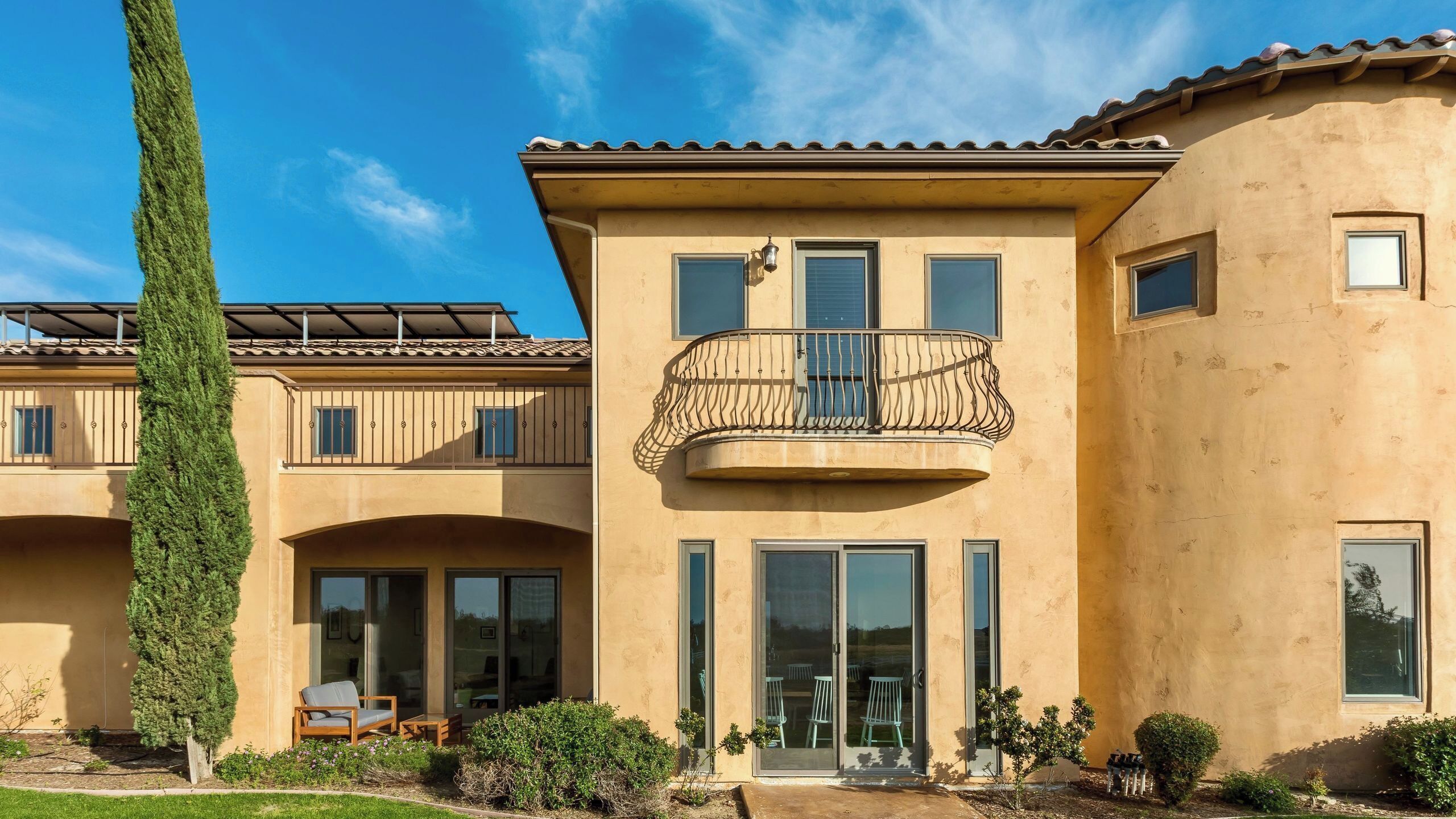 A multi-story building with a balcony, large windows, and a patio area.