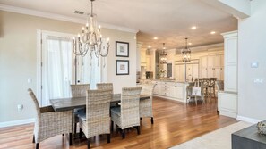 A spacious dining area with a chandelier, wicker chairs, and a large island with a sink. - Grand Contento by Avantstay Extraordinary Estate w/ Pool & Movie Room (Temecula)