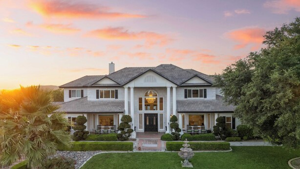 A large, stately house with a symmetrical facade, a central entrance, and a well-manicured garden with a fountain.