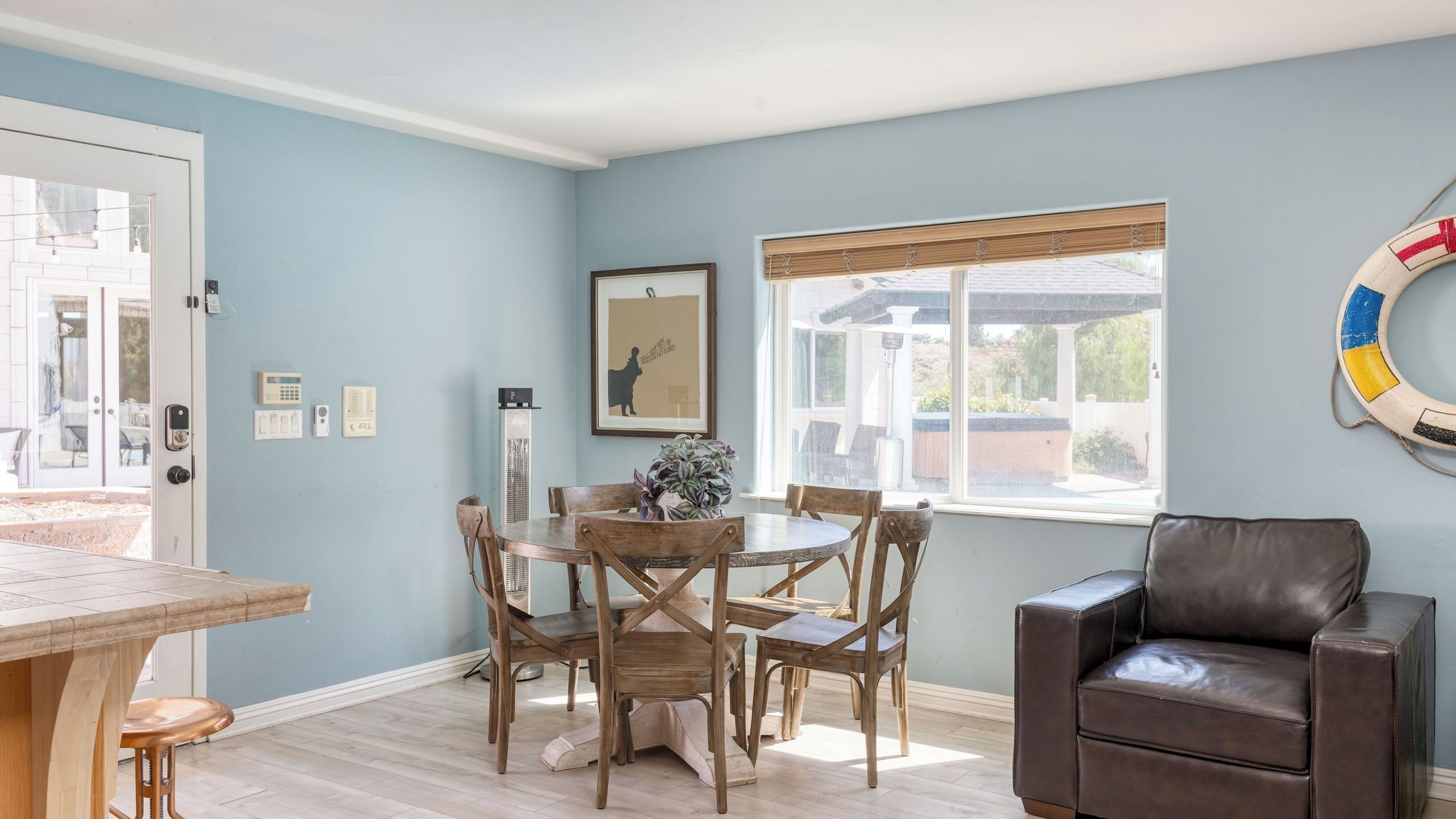 A dining area with a wooden table and chairs, a window with a view, and a lifebuoy on the wall.