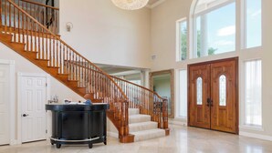 A spacious foyer with a grand staircase, a chandelier, and a large wooden door.