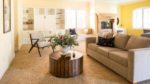 A living room with a beige sofa, a round wooden coffee table, and a white cabinet with shelves. - Amarilla by Avantstay Peaceful Paradise w/ Pool, Spa & Theatre Room (La Quinta)