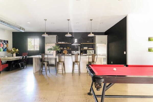 A modern kitchen with a central island, bar stools, pendant lighting, and a pool table.