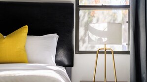 Ein ordentlich bezogenes Bett mit weißen und gelben Kissen, einem schwarzen Kopfteil und einem Nachttisch mit einer goldfarbenen Lampe.