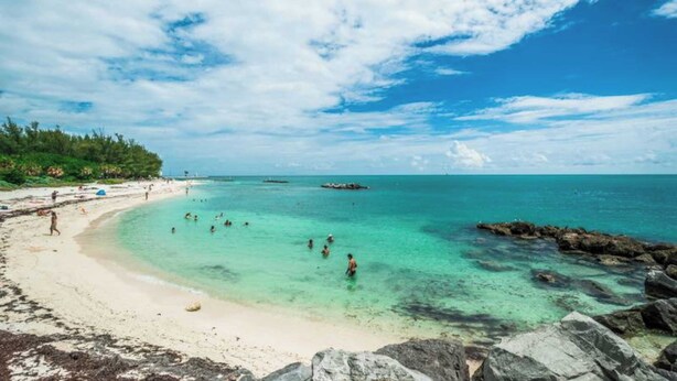 Een strand met helder turquoise water, een rotsachtige kustlijn en mensen die zwemmen.