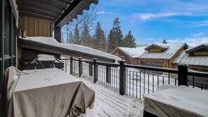 Ein mit Schnee bedeckter Balkon mit Tisch und Stühlen, der auf eine verschneite Landschaft und Gebäude blickt.