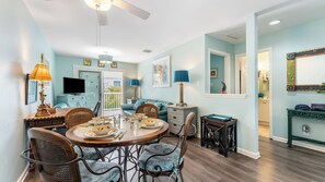 A dining area with a round table, chairs, and a television. There is a balcony with a railing and a door leading outside. - A Siesta Bay by Avantstay Key West Walkable Gated Community, Shared Pool Month-long Stays (Key West)