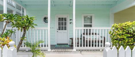 A light blue house with a white porch, a door, and a small table with chairs.