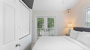 A bedroom with a bed, a nightstand, a lamp, and a view through a door to a balcony. - Coral Breeze by Avantstay Close to Beach w/ Balcony & Shared Pool! Month Long Stays Only (Key West)
