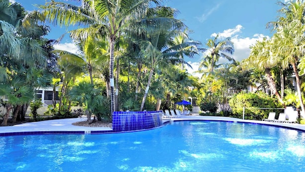A swimming pool with blue tiles, surrounded by palm trees and lounge chairs. - Coral Breeze by Avantstay Close to Beach w/ Balcony & Shared Pool! Month Long Stays Only (Key West)