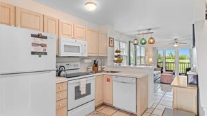 A modern kitchen with wooden cabinets, a white refrigerator, a microwave, an oven, and a dishwasher. There is a window with a view of greenery outside. - Coral Breeze by Avantstay Close to Beach w/ Balcony & Shared Pool! Month Long Stays Only (Key West)