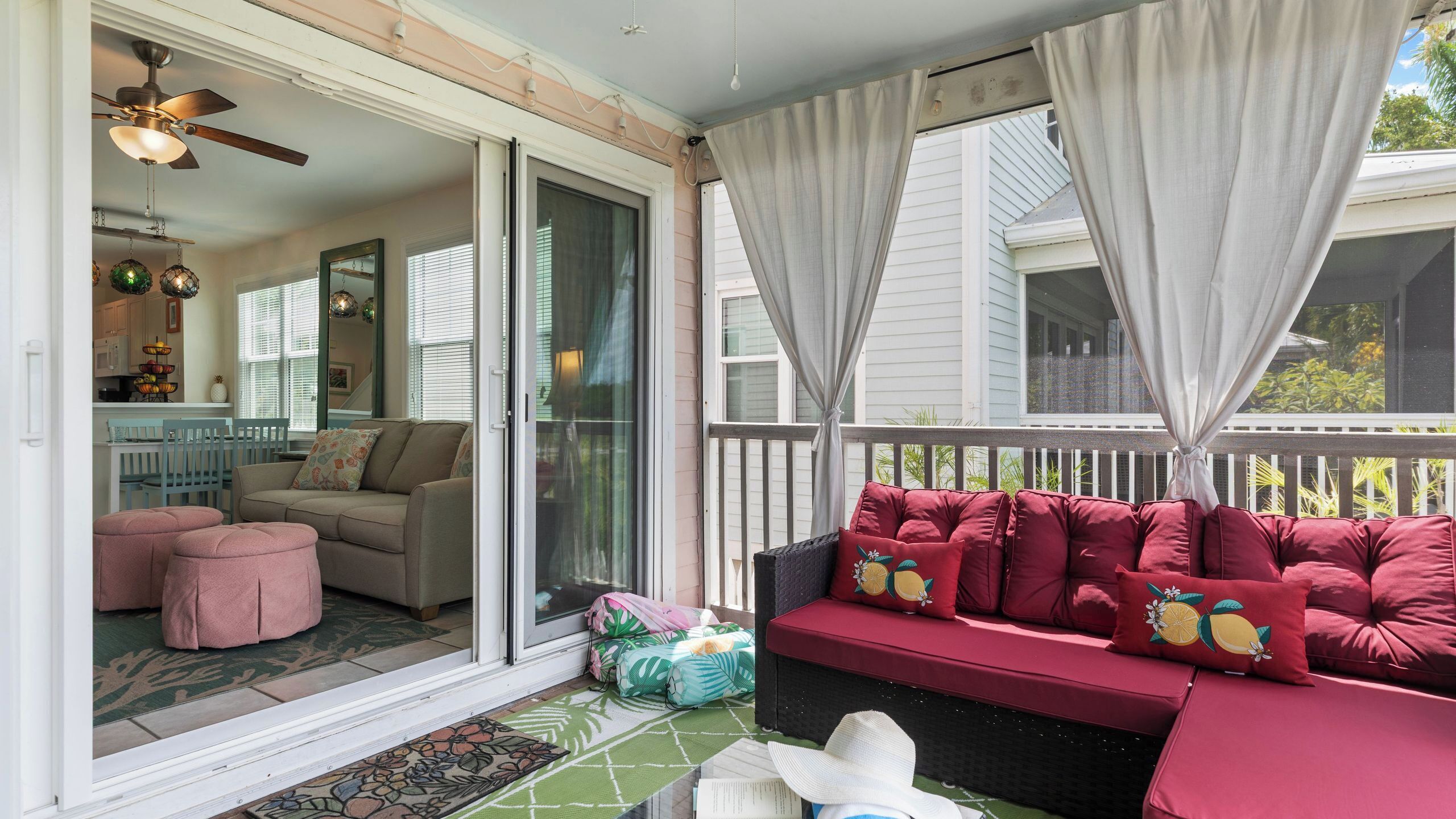 A covered porch with a sliding glass door leading to a living room, a ceiling fan, and a dining area with a kitchen visible through the door.