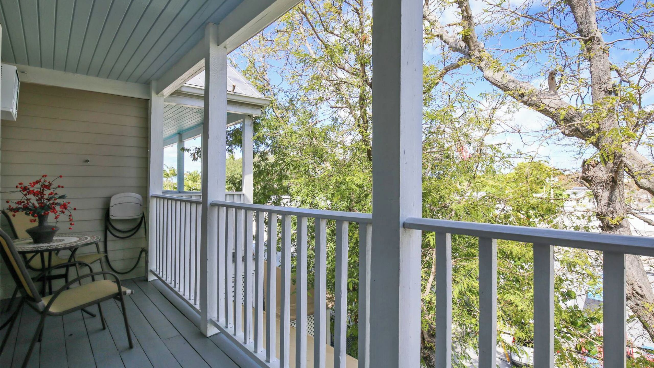 A covered porch with a railing, a table with chairs, and a potted plant.