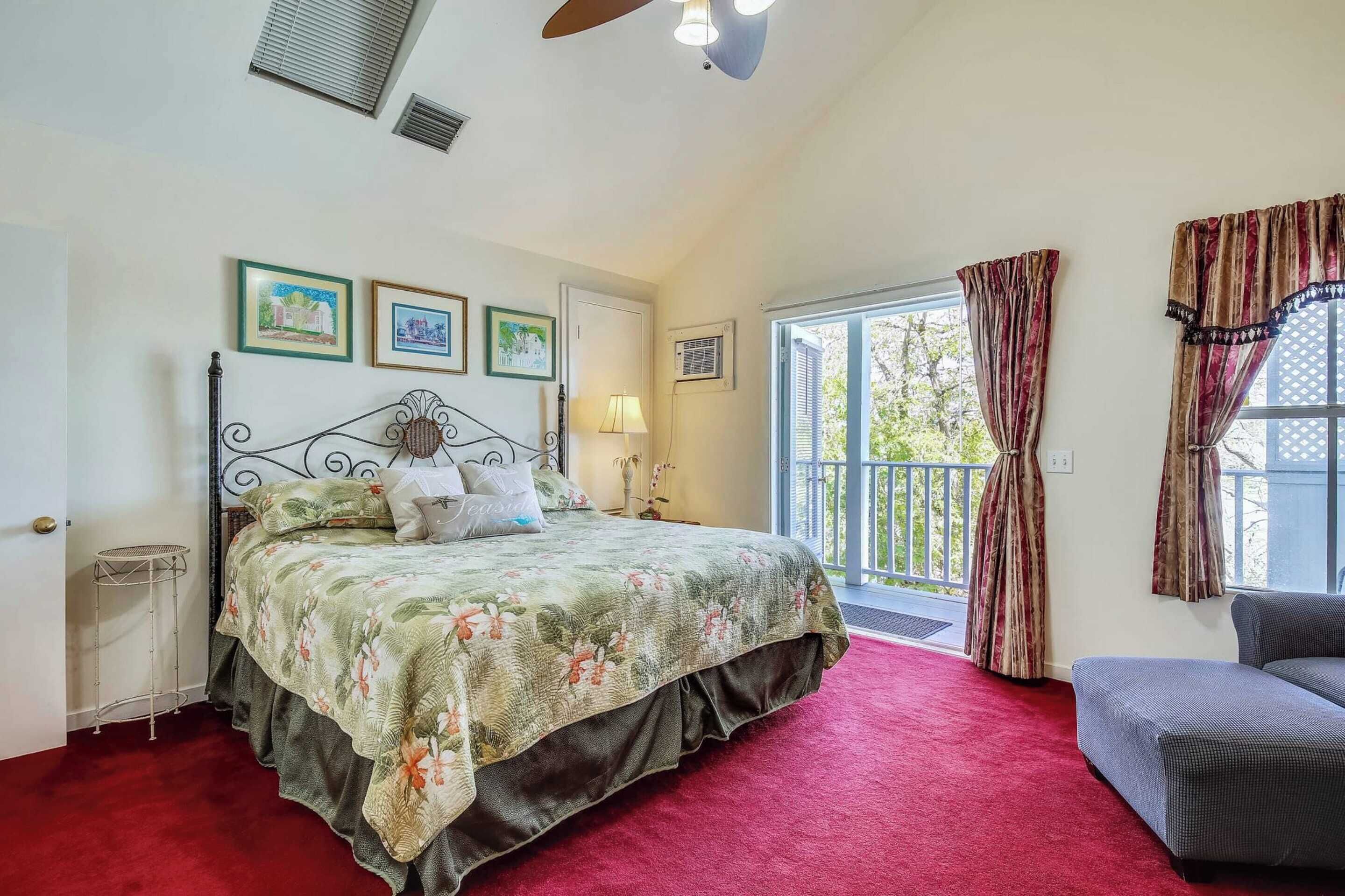 A bedroom with a bed, a window with curtains, a balcony, and framed pictures on the wall.
