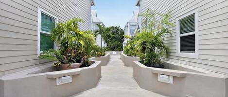 A narrow pathway flanked by two buildings with potted plants and a clear sky.