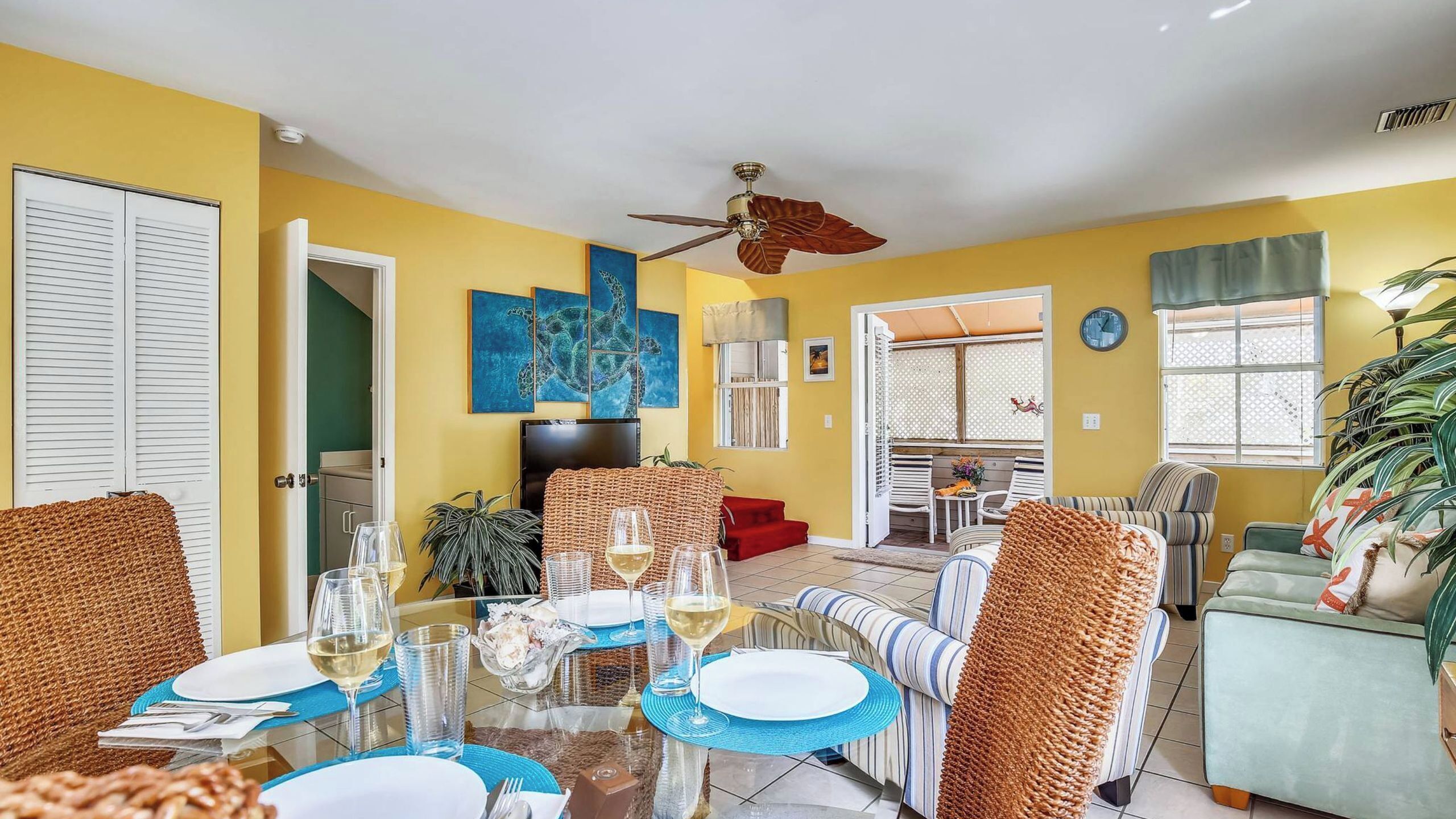 A dining area with a table set for two, a ceiling fan, and a view into the living room.