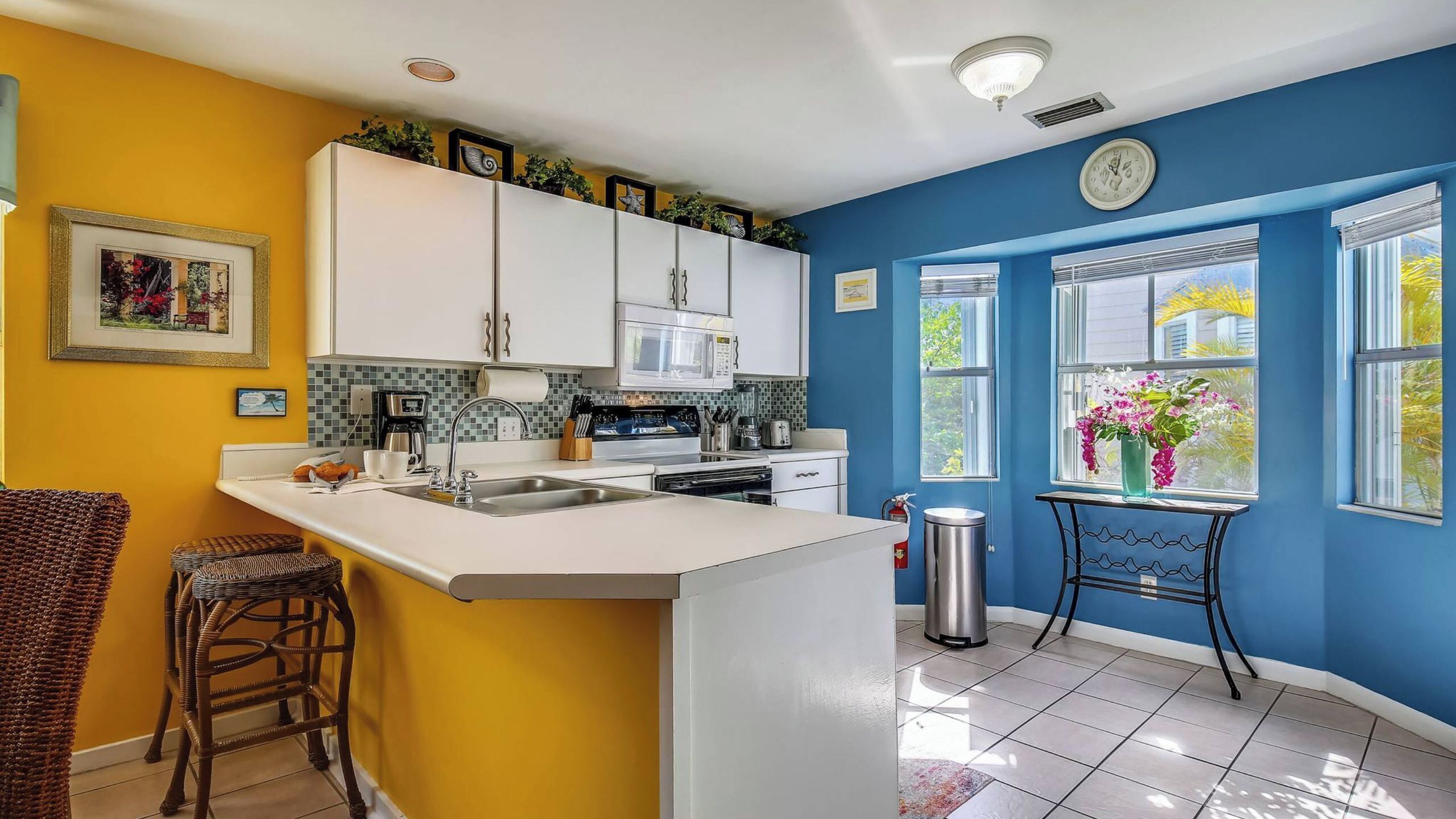 A kitchen with white cabinets, a microwave, and a sink. There is a window with a view of trees and a vase with flowers.