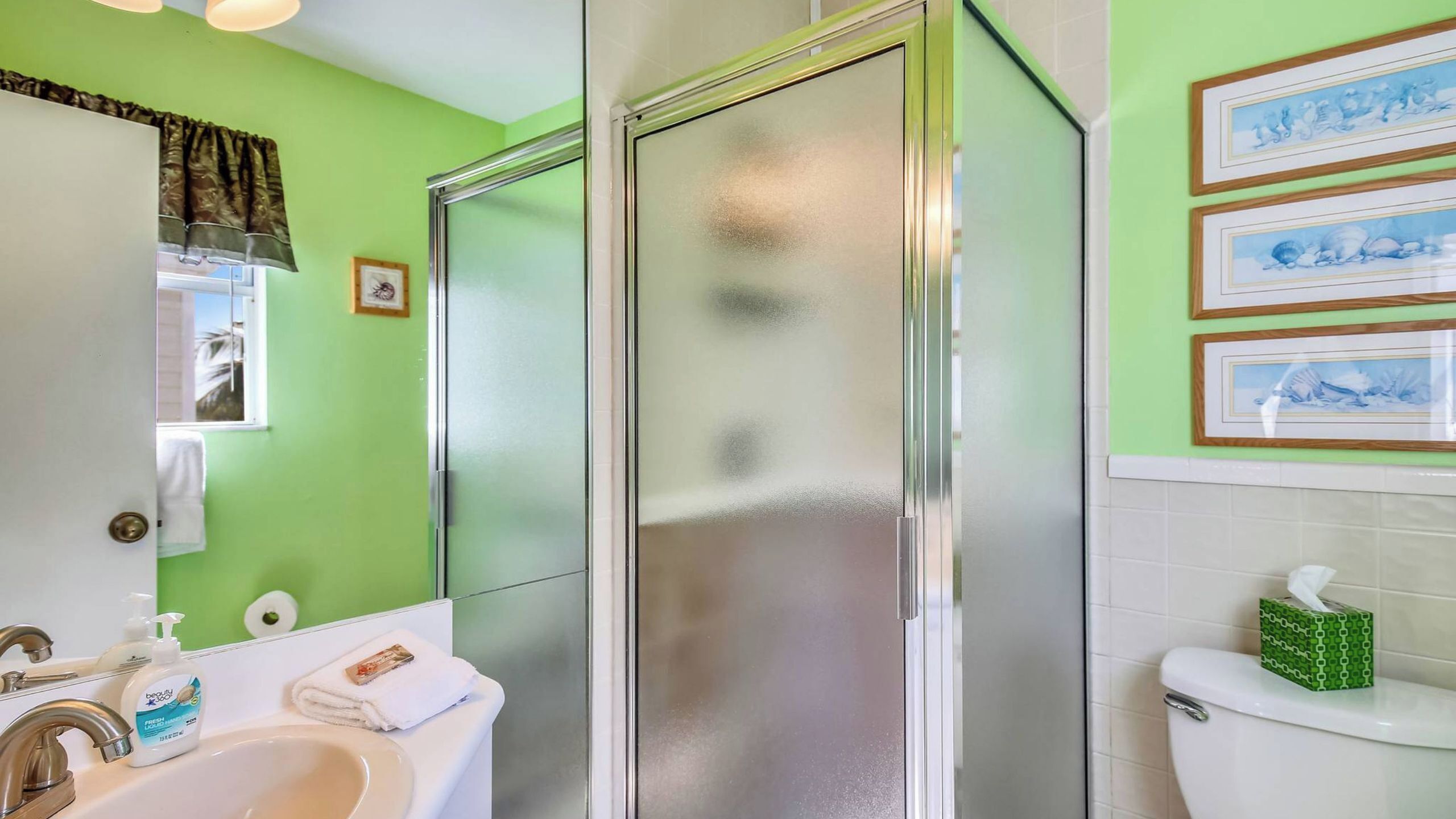 A bathroom with a shower, sink, toilet, and green walls.