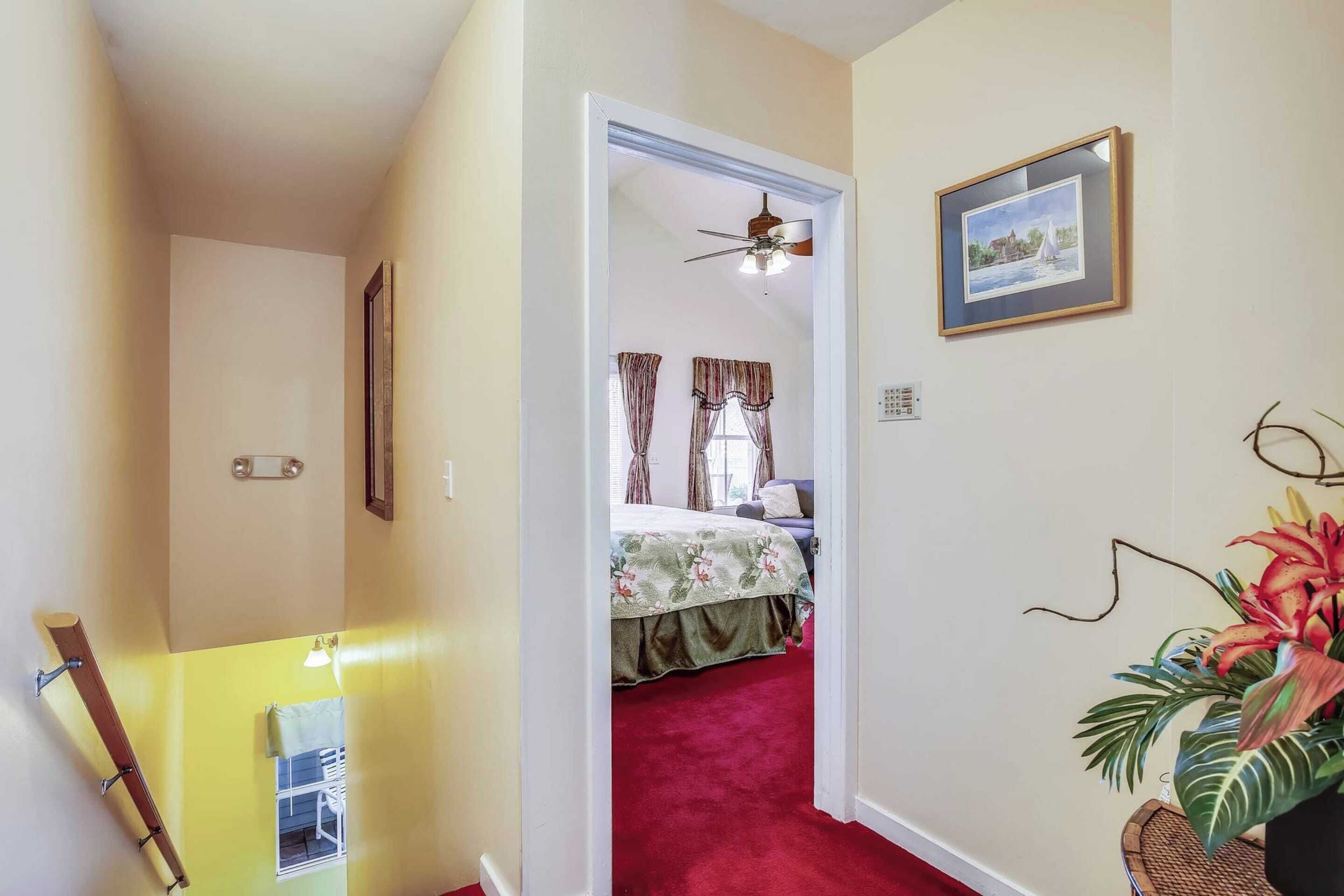 Un corridoio con tappeto rosso che conduce a una camera da letto con letto, tende e ventola a soffitto.