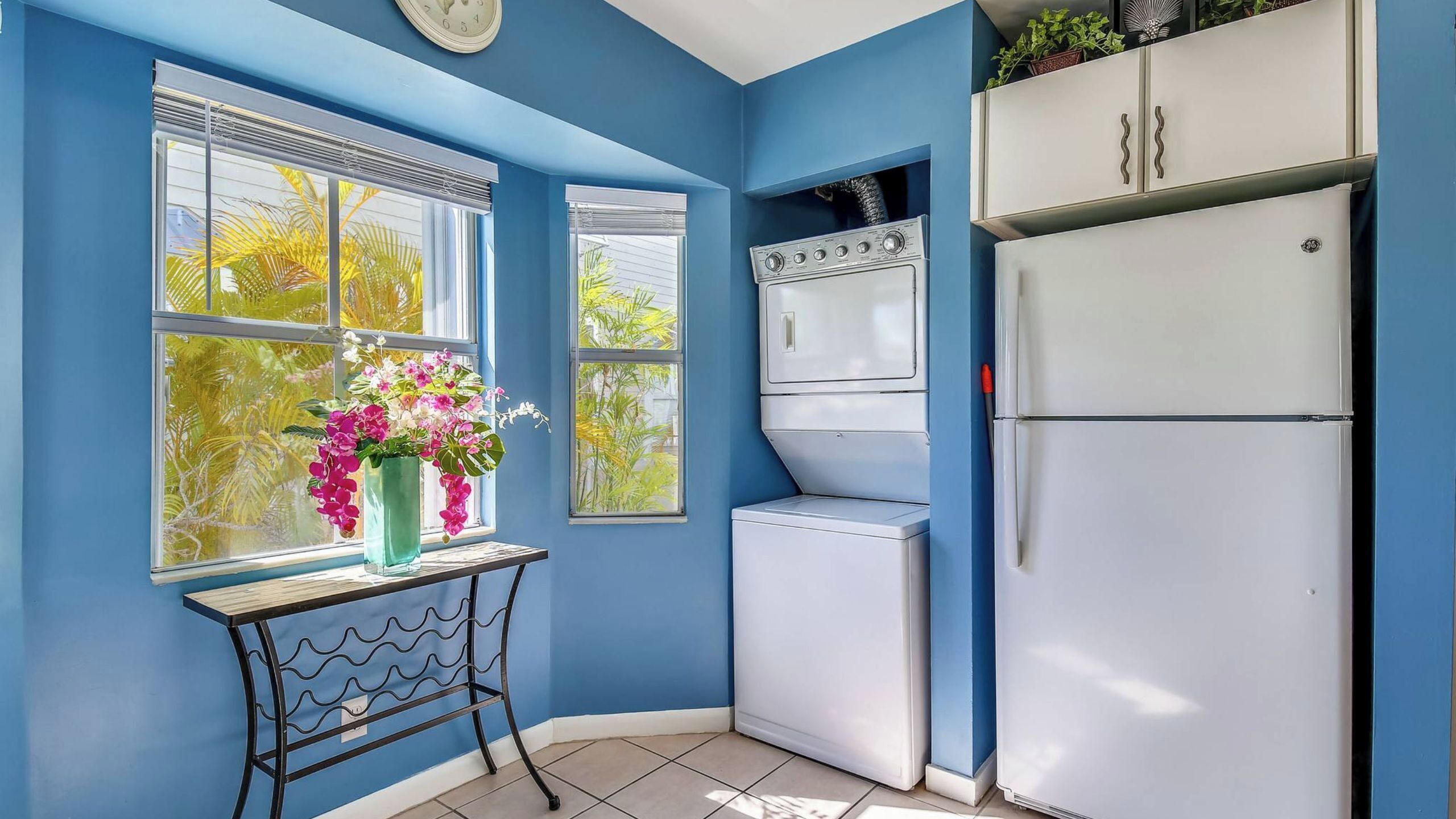 Une cuisine avec des murs bleus, un réfrigérateur blanc, un lave-linge et une horloge au mur.