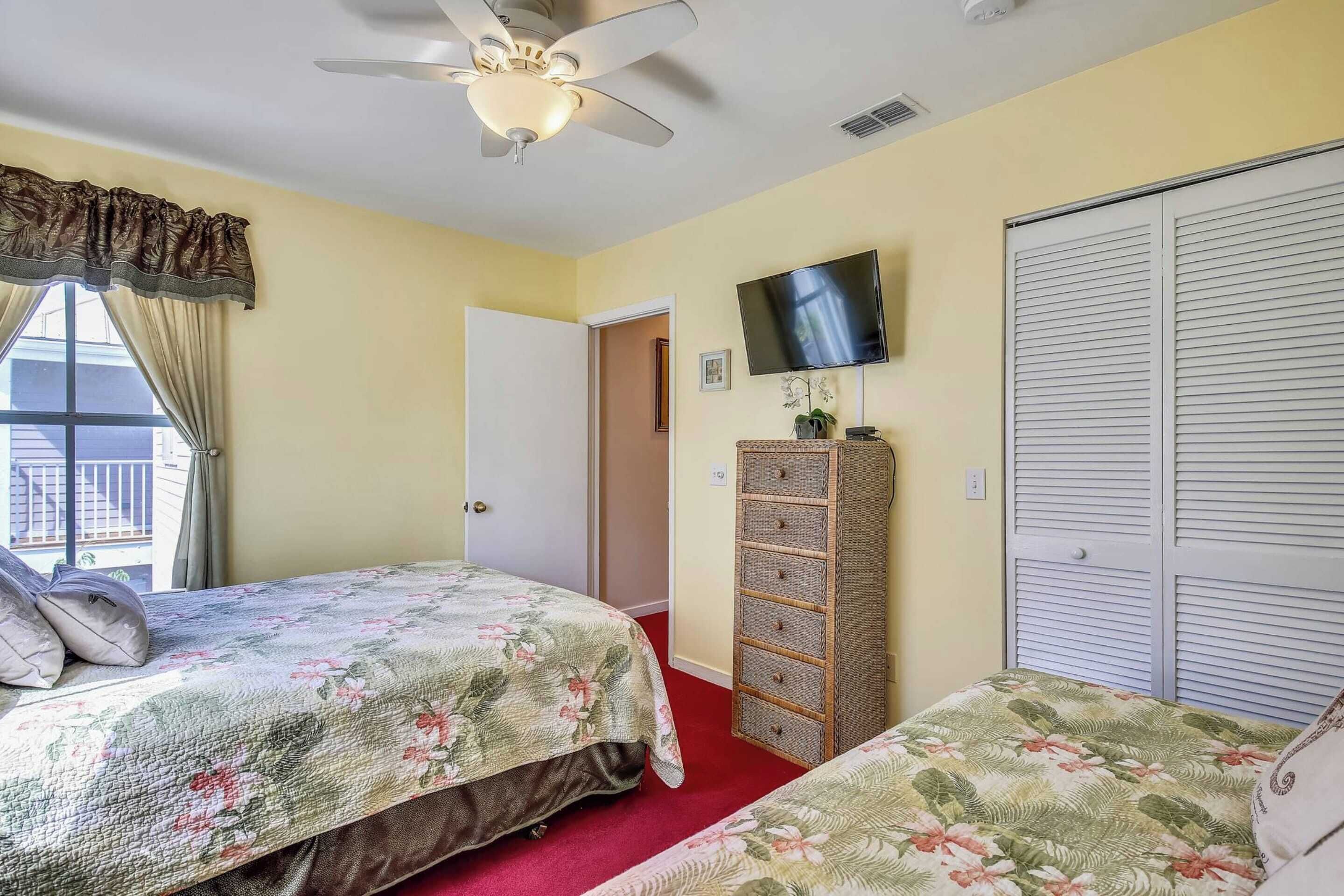 A bedroom with two beds, a ceiling fan, a TV, a wardrobe, and a window with curtains.