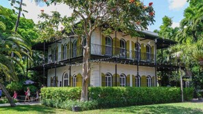 A two-story building with a balcony, surrounded by lush greenery and palm trees. - Southard Getaway by Avantstay w/ Covered Patio, Great Location & Shared Pool! Month Long Stays (Key West)