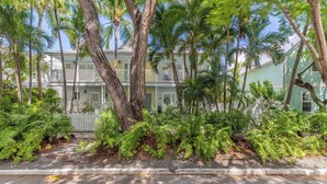 A multi-story building with balconies, surrounded by lush greenery and a white picket fence. - Southard Getaway by Avantstay w/ Covered Patio, Great Location & Shared Pool! Month Long Stays (Key West)