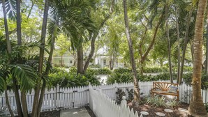 A white picket fence, a pathway, and a bench in a lush garden with tall trees. - Southard Getaway by Avantstay w/ Covered Patio, Great Location & Shared Pool! Month Long Stays (Key West)
