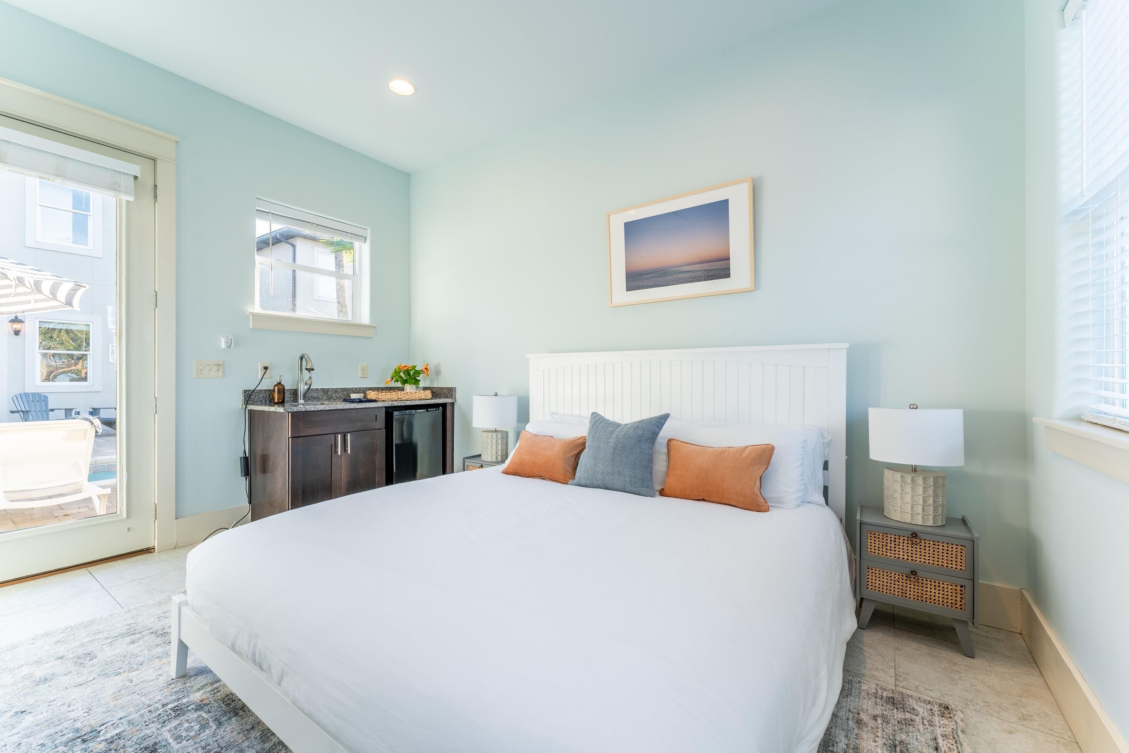 A bedroom with a large bed, a nightstand with a lamp, a window, and a view of the outside.