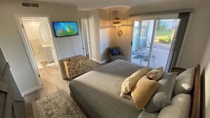 A bedroom with a large bed, a television, and a sliding glass door leading to an outdoor area.