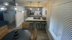 A modern kitchen with a central island, pendant lighting, and a dining area with a round table and chairs.