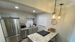 A modern kitchen with stainless steel appliances, a marble countertop, and bar stools.